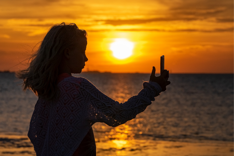 夕焼けを背景に写真を撮る女の子